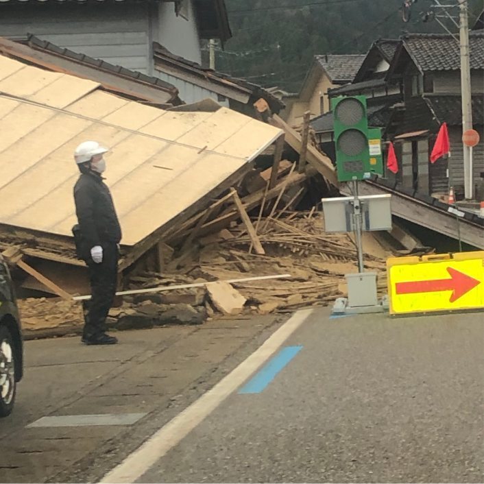 Rescuer wearing face mask standing on road in front of a collapsed building in Japan.