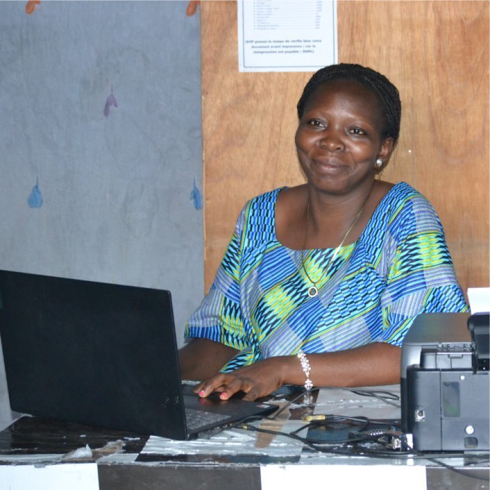 A Congolese woman dressed in a blue top sitting behind a desk
