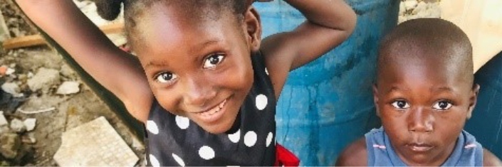 Two haitian children smiling into the camera one a little girl and the other her younger brother