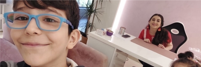 Close up of a young boy wearing blue eye glasses and another girl in the scene behind him