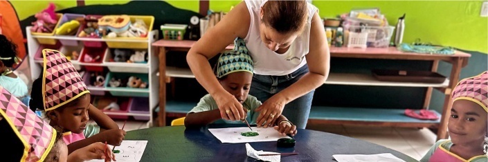 Teacher helping young Haitian student with desk work while other students are at desk
