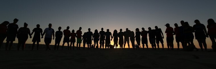 A silhouette of people in a line in front of a sunset