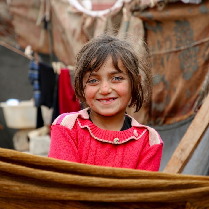 Young refugee girl dressed in red smiling at camera