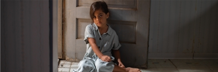 young girl sitting on the floor in a bare room with a sad expression on her face