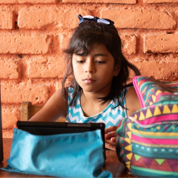 Honduran girl sitting a table with school bags in front of her reading a book.