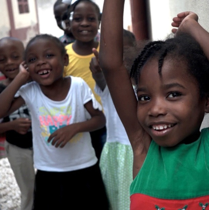 Smiling Haitian girl with arms waving in the air smiling playmates in the background