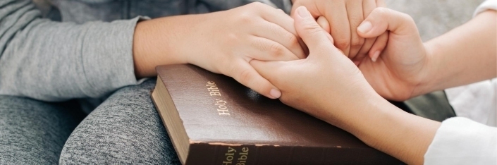 Two sets of hands holding each other on top of a brown Bible.