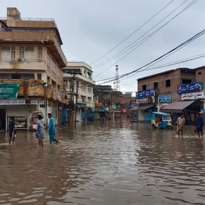 City street in Shikarpur with floodwaters covering all roads people walking in muddy water