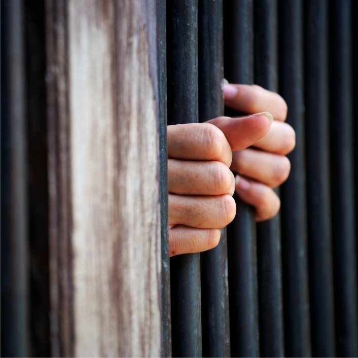 Hands coming from a prison cell gripping the bars.
